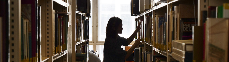 Mujer cogiendo libros en una de las estanterías de la biblioteca en la Facultad de Filosofía y Letras